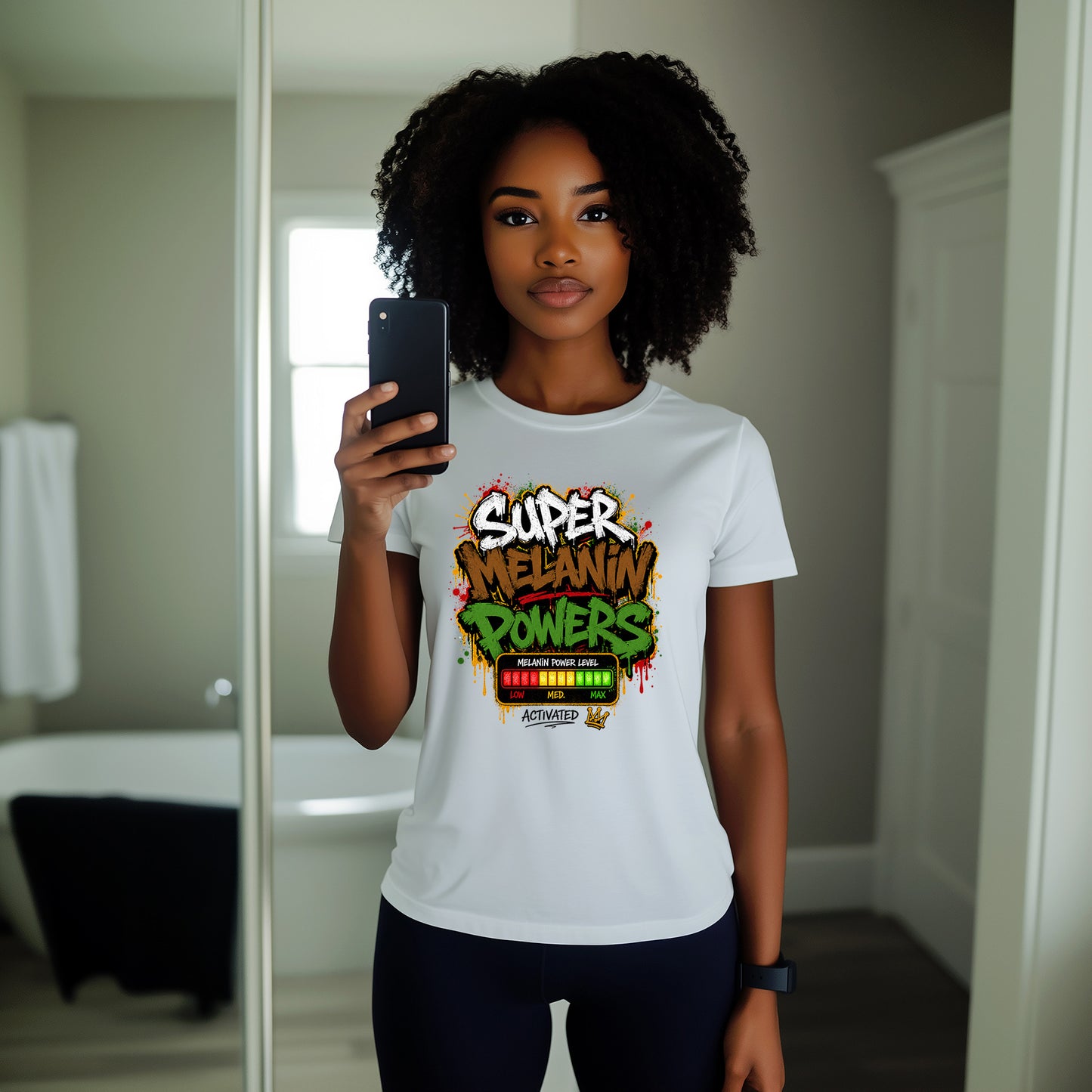 A woman taking a mirror selfie in a bathroom, wearing a white graphic t-shirt with a colorful 'SUPER MELANIN POWERS' design on the front.