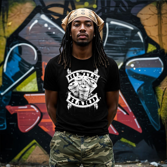 Person wearing a black t-shirt with 'Hustle Hard' graphic and camouflage pants in front of a graffiti wall.